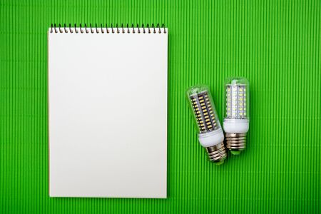 Energy saving LED light bulb with empty notepad on a green backgroundの写真素材