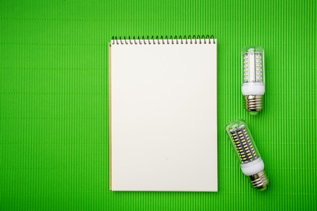 Energy saving LED light bulb with empty notepad on a green backgroundの写真素材