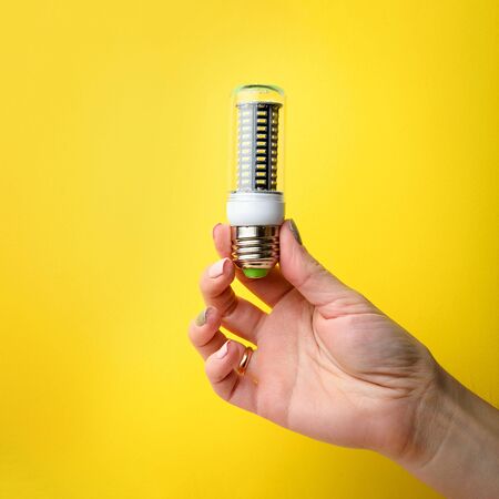 Hand holding LED bulb lamp on yellow background. Eco power concept.の写真素材