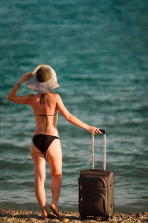 woman in swimsuit with suitcase on beachの写真素材