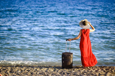 woman in red dress with suitcase seaの写真素材