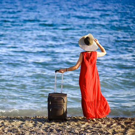 woman in red dress with suitcase seaの写真素材