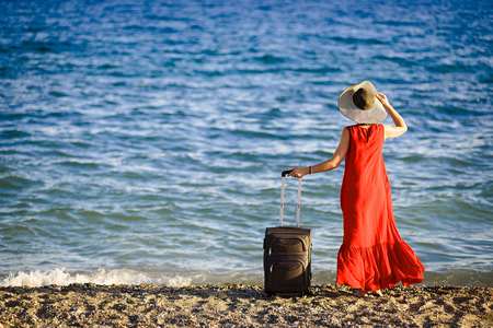 woman in red dress with suitcase seaの写真素材
