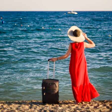 woman in red dress with suitcase seaの写真素材