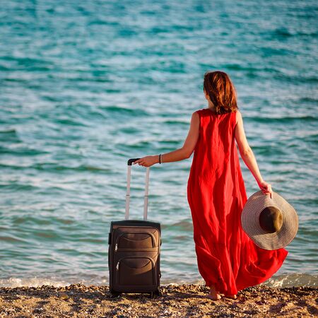 woman in red dress with suitcase seaの写真素材
