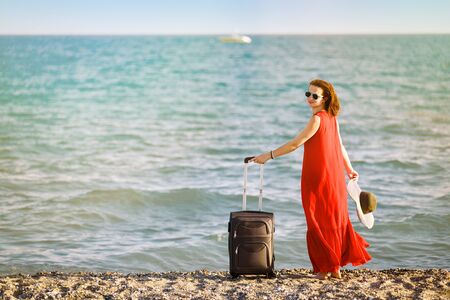 woman in red dress with suitcase seaの写真素材
