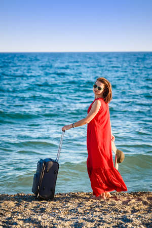 woman in red dress with suitcase seaの写真素材