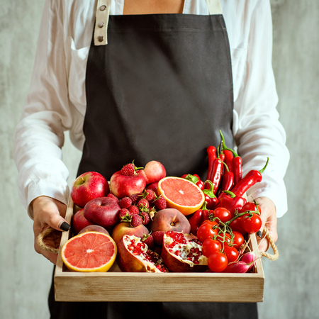 girl holds wooden tray with fresh red vegetables and fruits on grey background. Healthy eating vegetarian concept.の写真素材