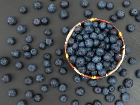 Blueberries in a ceramic bowl and on a black wooden table. Healthy blueberry snack. Fresh vegan breakfast. Close up. Bunch of vitamins.の写真素材