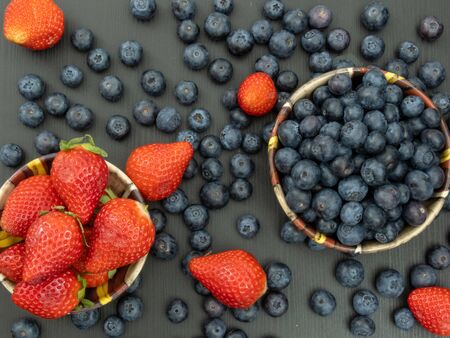 Blueberries and Strawberries in ceramic bowls and on a black wooden table. Healthy red berry snack. Fresh vegan breakfast. Close up. Bunch of vitamins.の写真素材