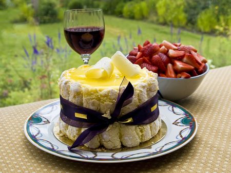 Lemon charlotte cake with glass of wine and a bowl of strawberry set on a table overlooking gardenの写真素材