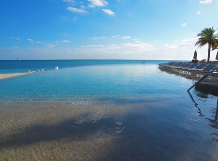 Infinity pool with deck chairs overlooks the ocean in a luurty resort settingの写真素材