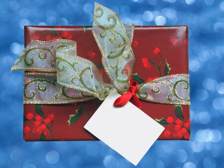 Christmas present box over blue blurred background, wrapped with ribbon and card     の写真素材