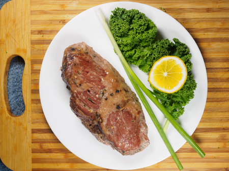 Braised beef brisket on a plate with kale and green onion, set on a wooden cutting board