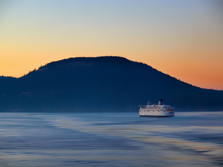 Ferry making its way by the island at the sunset timeの写真素材