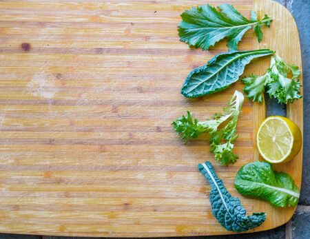 Leafy greens for a salad on  a cutting board. Kale, spinach, and lemon, with copy spaceの写真素材