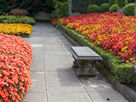 Bench on the walkway in the autumn garden among lush flower beds