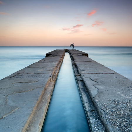 Digital manipulation showing a figure of an angel standing on a pier during a beautiful sunsetの写真素材