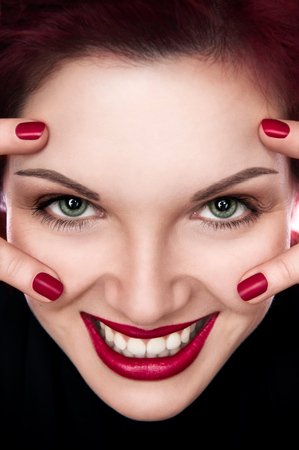 Closeup portrait of a young, beautiful girl with red hair, red lips and red nails smilingの写真素材