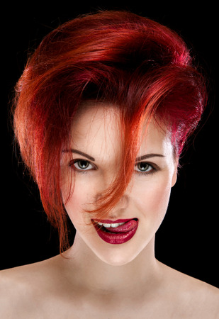 Portrait of a pretty girl with red hair and makeup showing her tongue in a studio on a black backgroundの写真素材