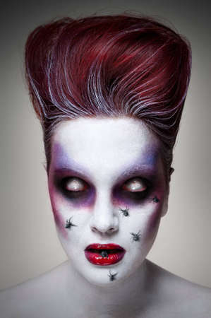 Portrait of an undead girl with red hair, white murky eyes, red lips and spiders crawling on her faceの写真素材