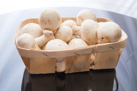 Champignon mushrooms in a basket on a glass tableの写真素材