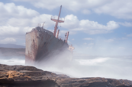 Abandoned, covered in rust shipwreck being hit with huge waves during a sea storm on Andros island in Greeceの写真素材