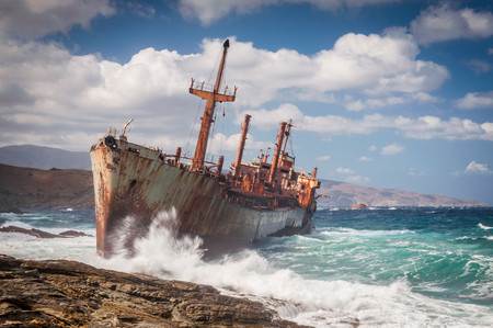 Abandoned, covered in rust shipwreck being hit with huge waves during a sea storm on Andros island in Greeceの写真素材