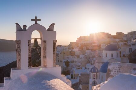 Church belfry in Firostefani during a sunset with the city and setting sun in the background, Santorini, Greeceの写真素材
