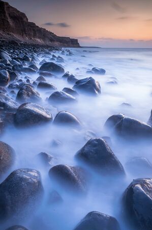 Long exposure shots of a rocky beach on northern peninsula of Santorini island in Greece during a sunsetの写真素材