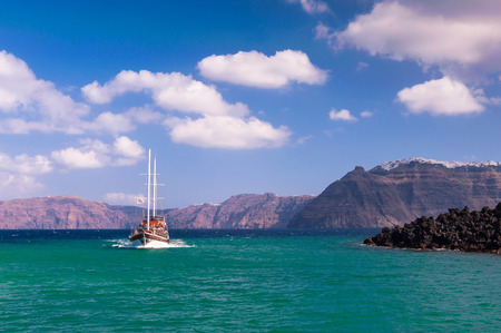 A sailing ship with tourists cruising between Nea Kameni volcano and Santorini island in Greece on a sunny dayの写真素材