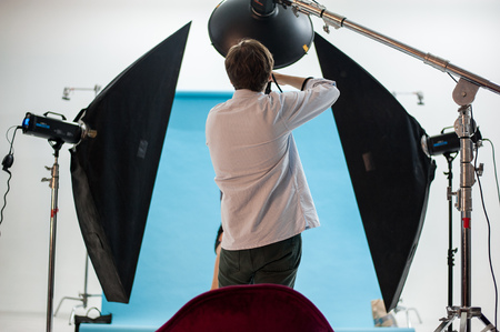 Backstage shot of a professional photoshoot in a studio with a model, photographer and light equipment.の写真素材