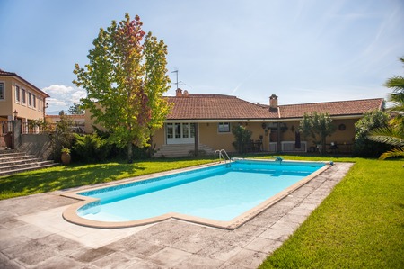 View on a luxury villa and a bright blue pool on a lawn. Shot on a hot summer sunny day with clear sky.の写真素材