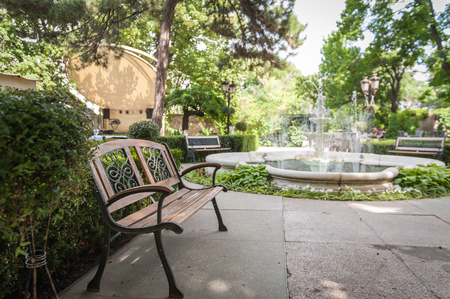 View on an old bench in the court yard of the House of Scientists in Odessa, Ukraine with a fountain in the background. Shot of sunny, summer day. No one in the shotの写真素材