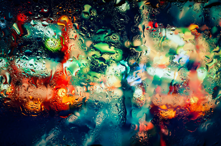 Blurry night city lights in the rain as seen through a wet glass with water dropletsの写真素材