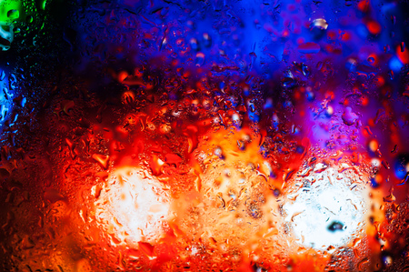 Blurry night city lights in the rain as seen through a wet glass with water dropletsの写真素材