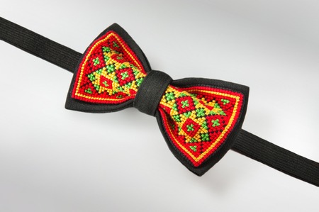 Studio shot of a stylish black bow-tie with a bright red, green and yellow ukrainian hand-made embroidery pattern on white backgroundの写真素材