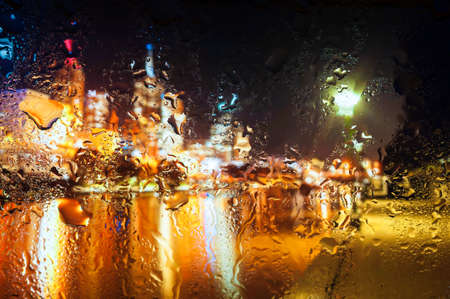 Blurry night city lights in the rain as seen through a wet glass with water dropletsの写真素材