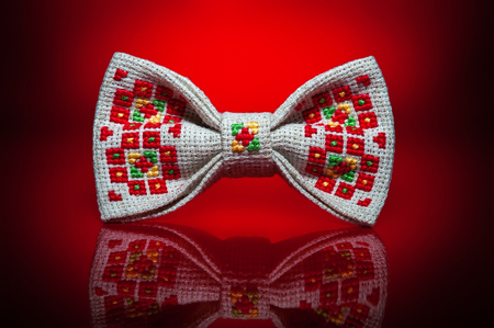 Studio shot of a stylish beige bow-tie with a bright red, green and yellow ukrainian hand-made embroidery pattern on red backgroundの写真素材