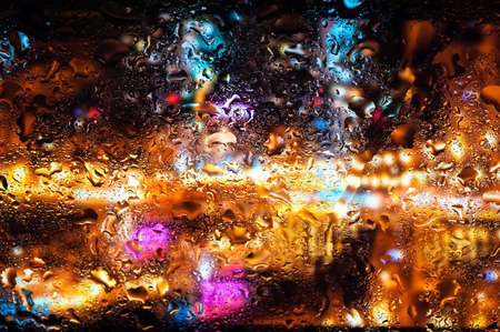 Blurry night city lights in the rain as seen through a wet glass with water dropletsの写真素材