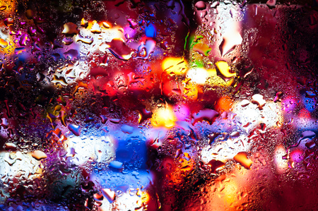 Blurry night city lights in the rain as seen through a wet glass with water dropletsの写真素材