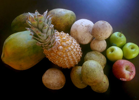A vibrant still life featuring fresh fruits, including apples, pineapples, papayas, and limes, arranged in a green bowl on a dark background. The colorful display highlights a rustの写真素材