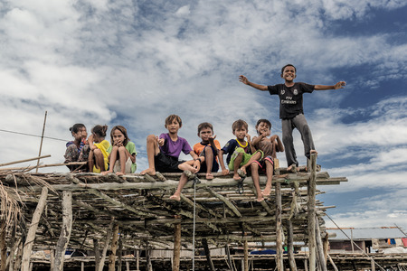 Bajau kids sitting on a wooden plank and showing hand gestures to tourist, Sabah Semporna, Malaysiaのeditorial素材