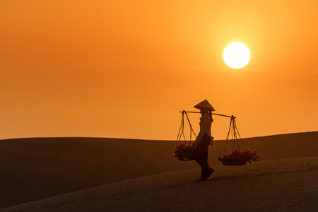 Woman carrying flower basket at sunset in Mui Ne sand dune, Vietnamの写真素材