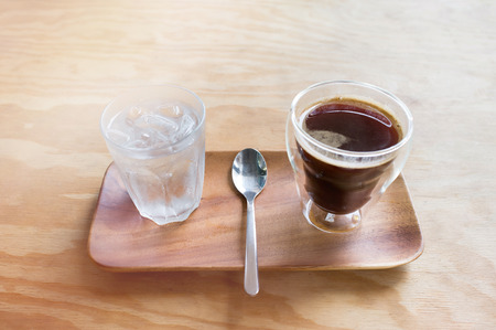 Hot Americano coffee with fresh water on wooden plate and wooden tableの写真素材