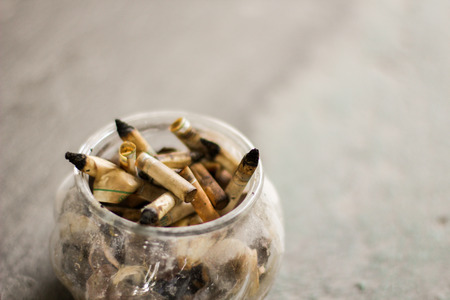 smoked cigarettes butts in the glass ashtray with grey backgroundの写真素材