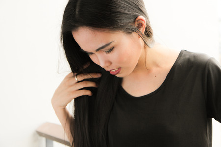 Portrait of a young smiling long hair asian woman, looking down and playing with her hair, white backgroundの写真素材