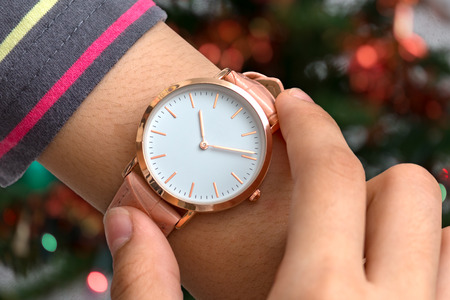 Girl's hand with wrist watch in Christmas time in front of Christmas tree in backgroundの写真素材