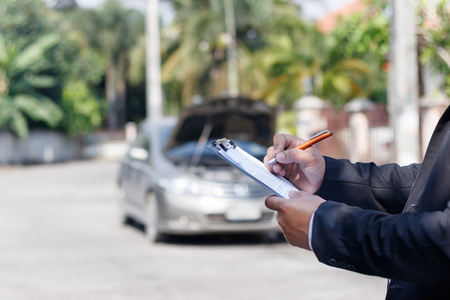 Side view of writing on clipboard while insurance agent examining carの写真素材