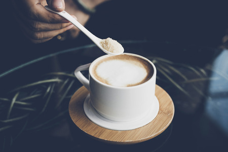 Woman's hands holding spoon with latte coffee on the table.の写真素材